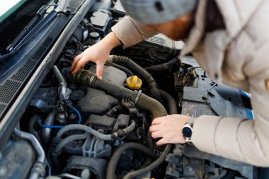 A lone man stands beside a broken-down car, looking worried working to repair the damage and get the vehicle back on the road