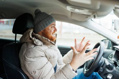 Angry driver in a traffic jam. He screams and gesticulates, Furious man gesticulates with hands and horns driving on traffic jam. Crazy driver yelling from car desperately.