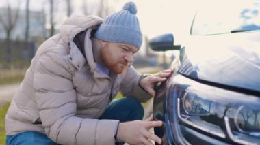 Contemplation and despair a young adult man stands beside a broken scratches car, clearly frustrated and displeased