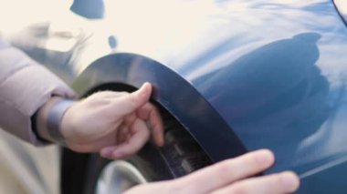 A close-up shot of a male hands, as he examines a scratch on his car, likely from a recent accident.