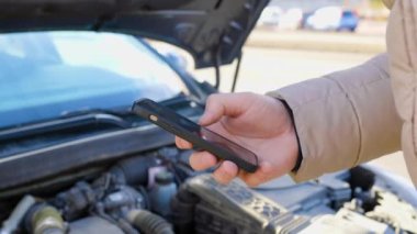 close up hands, A driver frantically making a call for assistance on his mobile phone, as he examines the damaged engine of his broken car