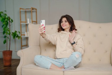 Closeup image of a beautiful woman waving hands while using mobile phone for video call at home. High quality photo