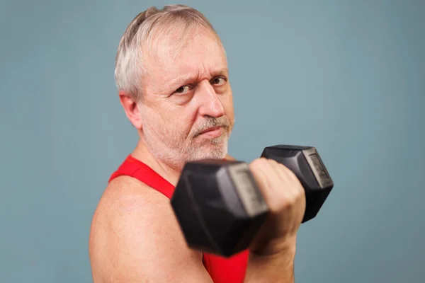 Senior man proves fitness knows no age This image captures a male senior citizen who is both athletic and energetic. With dumbbells in hand and a comical expression, he looks directly at the camera