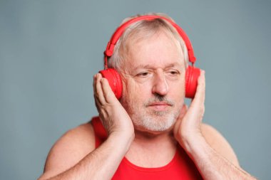 An elderly man brings humor to the studio, listening to music through his headphones, with a big smile of satisfaction. Blue background adds a modern touch to this comical scene.