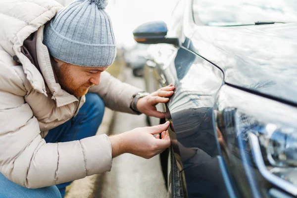 Examining the damage a man looks at a car with scratches, the result of a recent accident