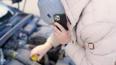 A young man examines the damage engine car, looking dejected as he talks on his mobile phone, likely trying to find help for his vehicle breakdown.