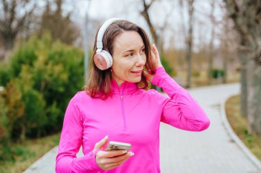 This authentic snapshot features a young and sporty woman enjoying a quiet moment of reflection and solitude. With her headphones and smartphone, shes able to stay connected