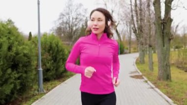 A pretty brunette runner jogging along a parkway on a beautiful day, her headphones on and her smartphone in hand, tracking her progress and staying motivated.