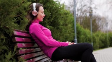 A beautiful young woman, with brunette hair, sits alone in the parkway, enjoying the sunshine and listening to music through her headphones. perfect embodiment of an active and carefree lifestyle