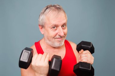 Energetic senior men proves fitness knows no age This studio shot features a male senior citizen with a sporty and energetic demeanor. Holding dumbbells and making a comical expression,