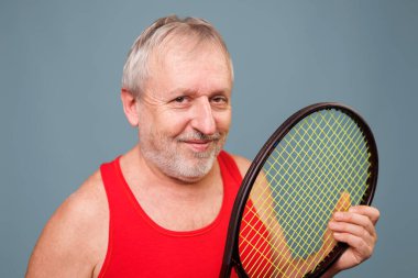 Satisfied Senior Sportsman with Tennis Racket This studio shot of a senior man, who is also a skilled tennis player, showcases his contentment as he holds his tennis racket with ease.