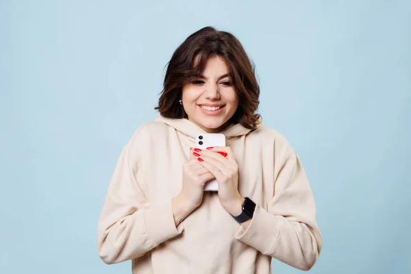 Şaşırmış güzel ergen bir kız heyecanla e-ticaret alışverişini bekliyor, elinde akıllı telefonu mavi bir arka planda. Stüdyo çekimi, kopyalama alanı
