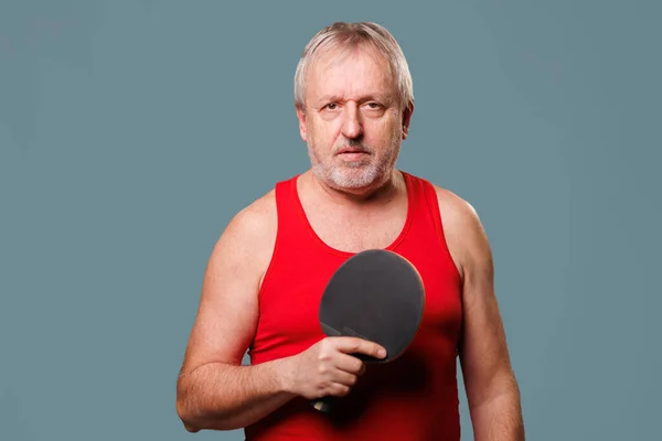 Elderly Man Playing Tennis This image showcases an older man who is still energetic and passionate about tennis. The man is seen holding a tennis racket, dressed in a red tank top,