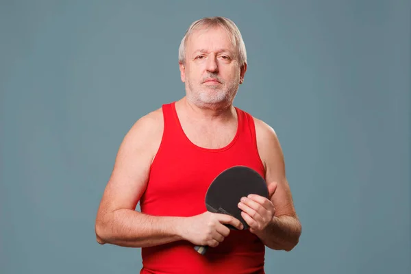 Active Pensioner with Tennis Racket This image features a senior man who is still active and athletic. The man is seen in the studio, with a blue background, and is holding a tennis racket,