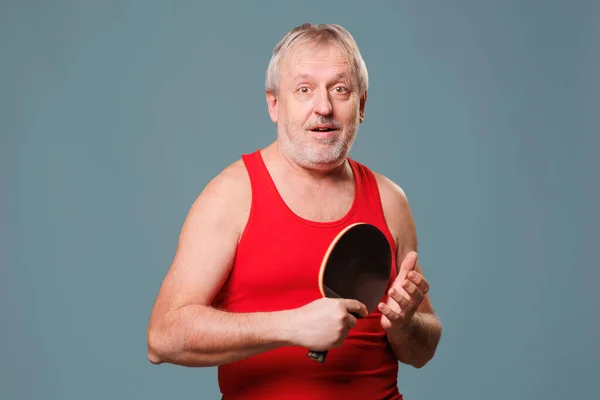 Older Sportsman with Tennis Racket This image showcases an elder man who still has a love for sports, especially tennis. The man is seen in the studio, with a blue background, and is holding a tennis