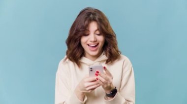 Genç bir kız mavi bir arka planda oturuyor, akıllı telefonundaki bir e-ticaret sitesine bakarken gülümsüyor ve heyecanlanıyor. Ürünlerin seçimi hayret verici ve ifadesi nefes kesici..