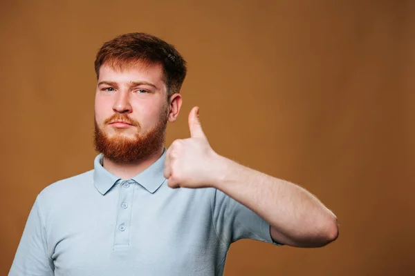 Genç, beyaz bir adam stüdyo ortamında kameraya gülümserken başparmağını kaldırıyor. Kızıl saçlı ergen bir erkek stüdyo çekimine onay vererek memnuniyetini ifade eder..