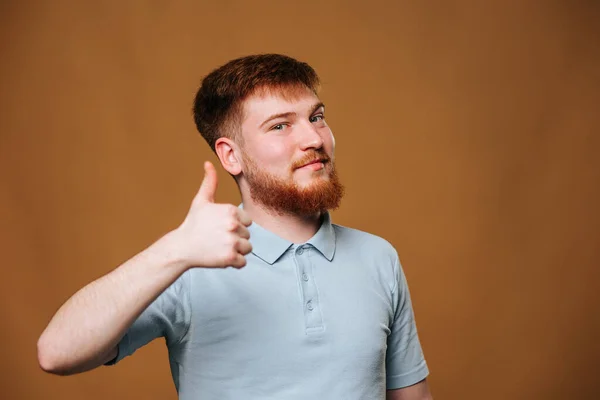 A teenage guy with a bright smile looks straight at the camera and gives a thumbs up in a studio setting. redhead teen shows his optimism and joy by flashing a thumbs up and smiling