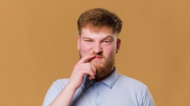 A hilarious studio shot of a young redhead guy looking at camera with a finger in nose and a funny expression. uncultured yet humorous photo of a male adolescent with a bored expression and finger