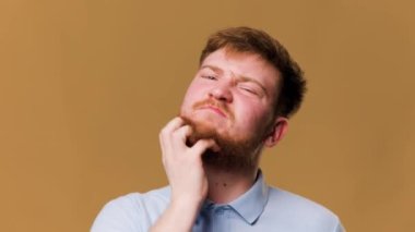 redhead guy in a studio shot, suffering from an allergic reaction and scratching his itchy hair desperately. unhappy-looking guy in a studio shot, suffering from itchy scalp and pulling on his hair