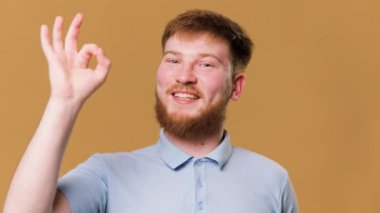 A young, caucasian guy gives a thumbs up while smiling at the camera in a studio setting. An adolescent male with red hair expresses his satisfaction by giving a thumbs up in a studio shot.