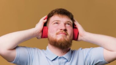 A teenage boy in a studio setting is fully immersed in his music, listening through headphones on his smartphone and making a hand gesture to show his enjoyment.