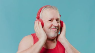 An older man finds joy in technology, as captured in this studio shot on a blue background of him using a smartphone and headphones to listen to music. satisfying seniors adapting to new devices.