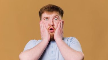 The teenage guy looks surprised and amazed as he strikes a pose in front of the camera in a studio. This adolescent male looks puzzled and shocked as he gazes into the camera lens during