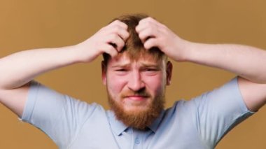 A studio shot of a guy with a head full of itchy hair, scratching his scalp in discomfort. young male with a worried expression on his face, constantly scratching his itchy hair in a studio shot.