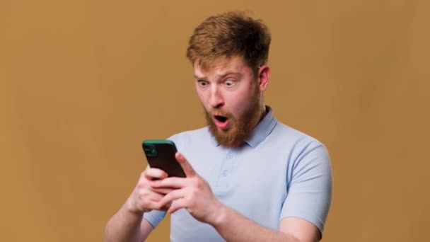 Shocked Teenage Guy Redhead Wearing Goggles Staring His Smartphone Studio — Stockvideo