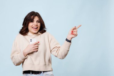 This teenage girls smiling face and pointing gesture towards the copy space in the background creates a playful and happy atmosphere in this studio shot, perfectly capturing the carefree spirit of