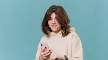 Tasasız, genç bir kadının cep telefonuyla dans edişinin belden yukarısında neşeli bir ifade var. Mavi arkaplanda izole edilmiş kameraya bakıyor müziğin ritmiyle..