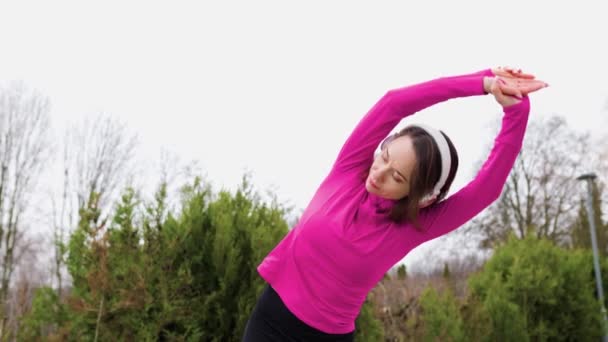 一个健康 活泼的高加索女人在公园里独自锻炼的时候 通过耳机听音乐 — 图库视频影像