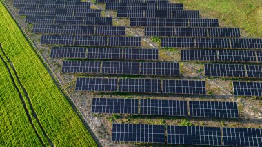 Güneş enerjisi parkının göz kamaştırıcı bir görüntüsü. Arkaplanı kayan tepeler ve doğal manzarayla dolu. Güneş panelleri düzenli sıralarda, teknoloji ve doğanın mükemmel karışımını temsil ediyor..
