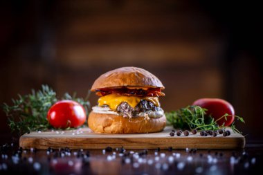 Çedarlı sığır burger, pastırma ve ahşap arka planda sos.