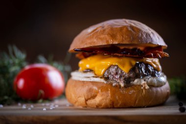 Çedarlı sığır burger, pastırma ve ahşap arka planda sos.