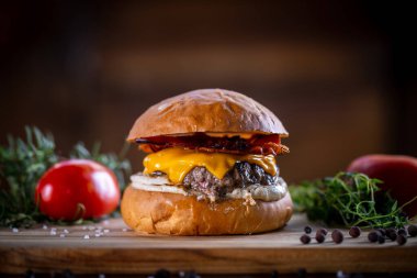 Çedarlı sığır burger, pastırma ve ahşap arka planda sos.