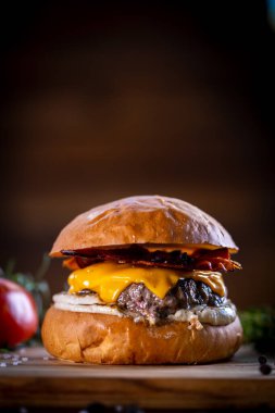 Çedarlı sığır burger, pastırma ve ahşap arka planda sos.