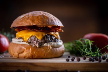 Çedarlı sığır burger, pastırma ve ahşap arka planda sos.