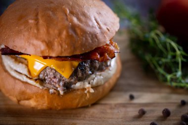 Çedarlı sığır burger, pastırma ve ahşap arka planda sos.