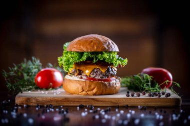Çedarlı sığır burger, pastırma, marul ve sos ahşap arka planda.