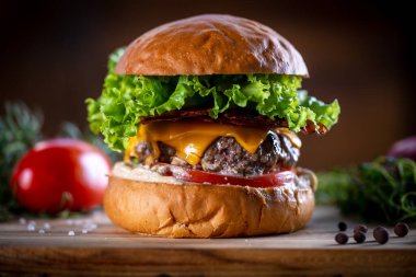 Çedarlı sığır burger, pastırma, marul ve sos ahşap arka planda.
