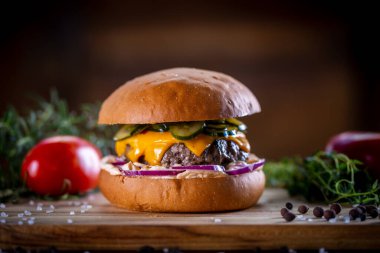 Çedarlı sığır burger, pastırma, turşu, mor soğan ve ahşap zemin üzerinde sos.