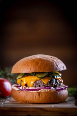 Çedarlı sığır burger, pastırma, turşu, mor soğan ve ahşap zemin üzerinde sos.