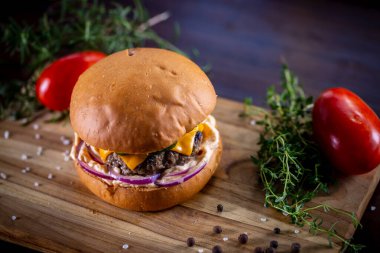 Çedarlı sığır burger, pastırma, turşu, mor soğan ve ahşap zemin üzerinde sos.