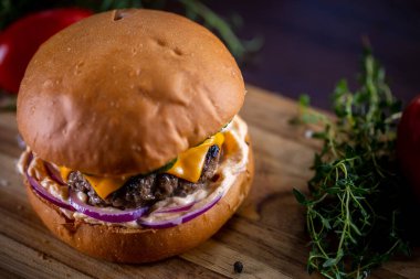 Çedarlı sığır burger, pastırma, turşu, mor soğan ve ahşap zemin üzerinde sos.