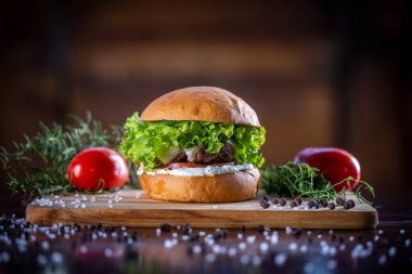 Peynirli sığır burger, marul, domates ve ahşap zemin üzerinde sos.