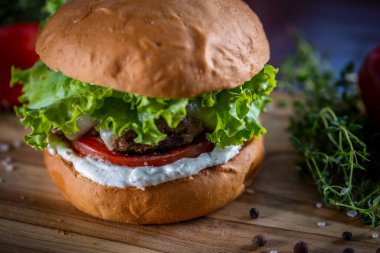 Peynirli sığır burger, marul, domates ve ahşap zemin üzerinde sos.