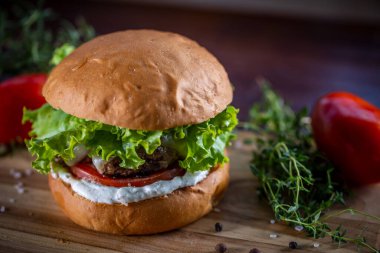 Peynirli sığır burger, marul, domates ve ahşap zemin üzerinde sos.