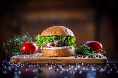 Peynirli sığır burger, marul, domates ve ahşap zemin üzerinde sos.